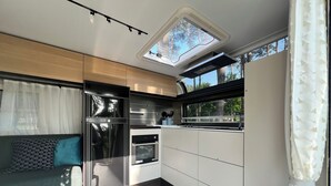 A compact kitchen with a built-in oven, a refrigerator, and a window overlooking greenery. - Luxury caravan 5 with whirlpool directly on the Achterwasser -holiday homes island Usedom (Lütow)