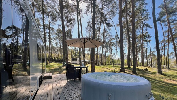 A hot tub on a wooden deck with a table and chairs, surrounded by a forest. - Luxury caravan 5 with whirlpool directly on the Achterwasser -holiday homes island Usedom (Lütow)
