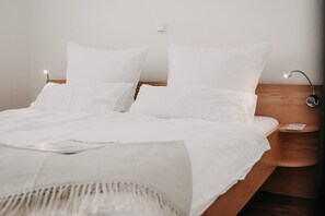 Cama bem arrumada com lençóis brancos, cabeceira de madeira e mesa de cabeceira com abajur.