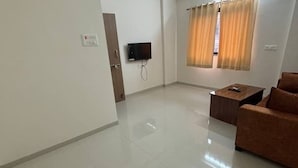 A clean, modern room with a flat-screen TV mounted on the wall, a small wooden table, and a brown sofa. - 1BHK Comfy Stay 4 (Pune)