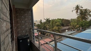 A balcony with a stone wall, a black object on the floor, and a view of palm trees and buildings in the background. - 1BHK Comfy Stay 4 (Pune)