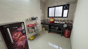 A compact kitchen with a refrigerator, stove, and various kitchen utensils. - 1BHK Comfy Stay 4 (Pune)