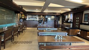 Un interior de restaurante con mesas y bancos de madera, una zona de bar y un techo alto con iluminación empotrada.