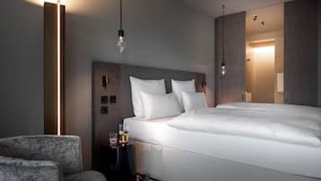 A modern hotel room with a large bed, a side table, a chair, and a wall-mounted light fixture.