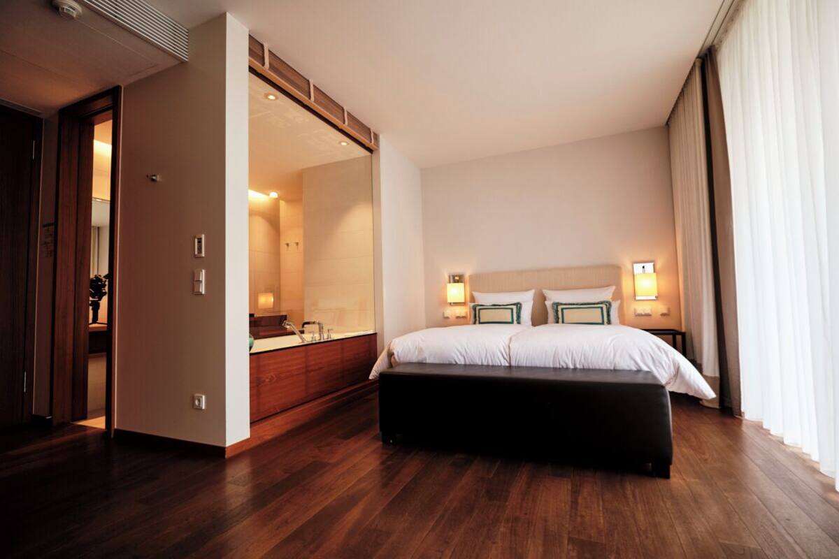 A hotel room with a large bed, bedside lamps, a mirror, and a wooden floor.