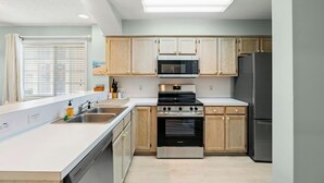 Une cuisine moderne avec des meubles en bois, un réfrigérateur en acier inoxydable, un four à micro-ondes et un four encastré.