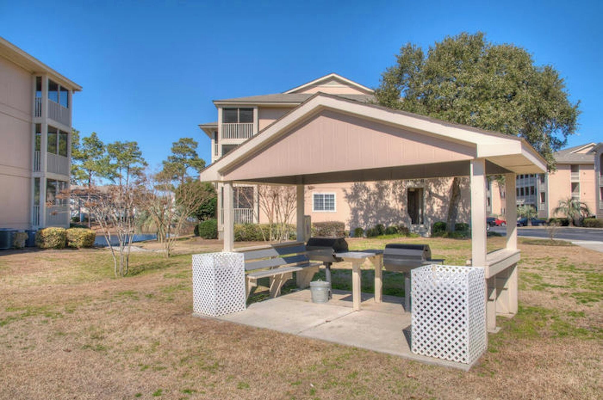 A covered outdoor seating area with a table and benches, surrounded by a fence, in a residential setting.