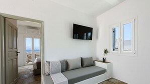 Un salón moderno con un sofá gris, un televisor montado y una ventana con vistas al mar.
