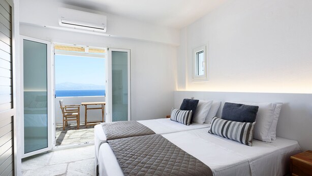 Un dormitorio con dos camas, un balcón con mesa y sillas, y vista al mar.