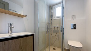 Un baño moderno con ducha de vidrio, inodoro blanco y tocador de madera con lavamanos.