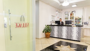 A hotel reception area with a tiled floor, a reception desk, a potted plant, and a star-shaped design on the floor. - Hotel Village (Pato Branco)
