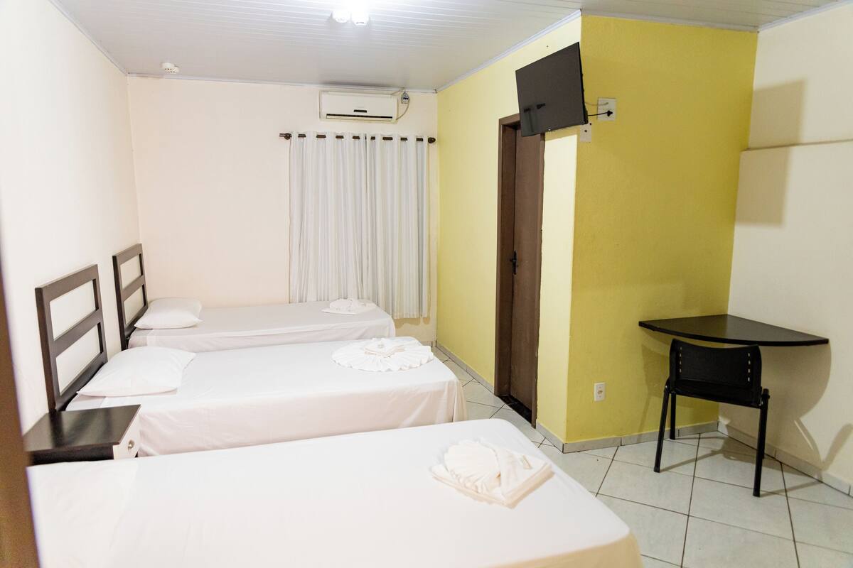 A hotel room with three single beds, a desk, a chair, and a door.