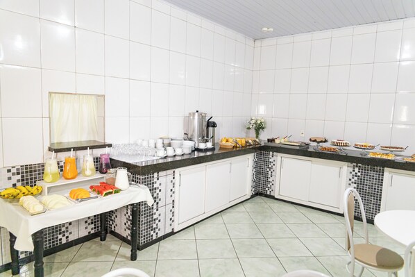 A kitchen with white tiled walls, a black and white tiled backsplash, a coffee maker, and a buffet with various food items. - Hotel Village (Pato Branco)