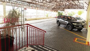 A covered parking area with a red railing, a black SUV, and a potted plant. - Hotel Village (Pato Branco)