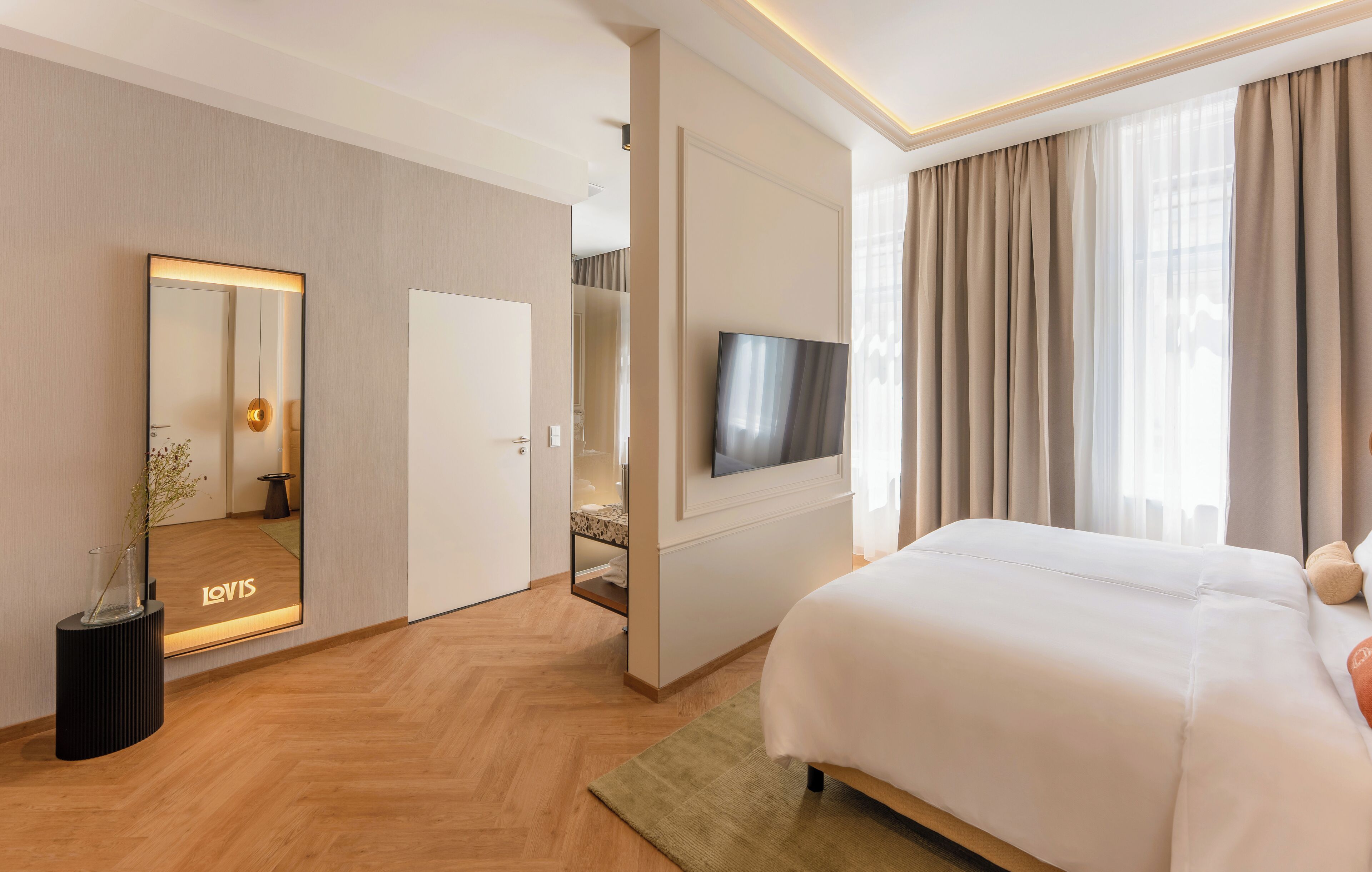 Una habitación de hotel moderna con una cama grande, un televisor de pantalla plana en la pared, un espejo con luz y vistas a la ciudad a través de amplios ventanales.