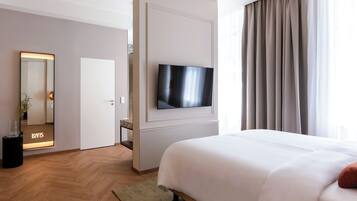 A hotel room with a bed, a TV mounted on the wall, a mirror, and a door leading to another room.