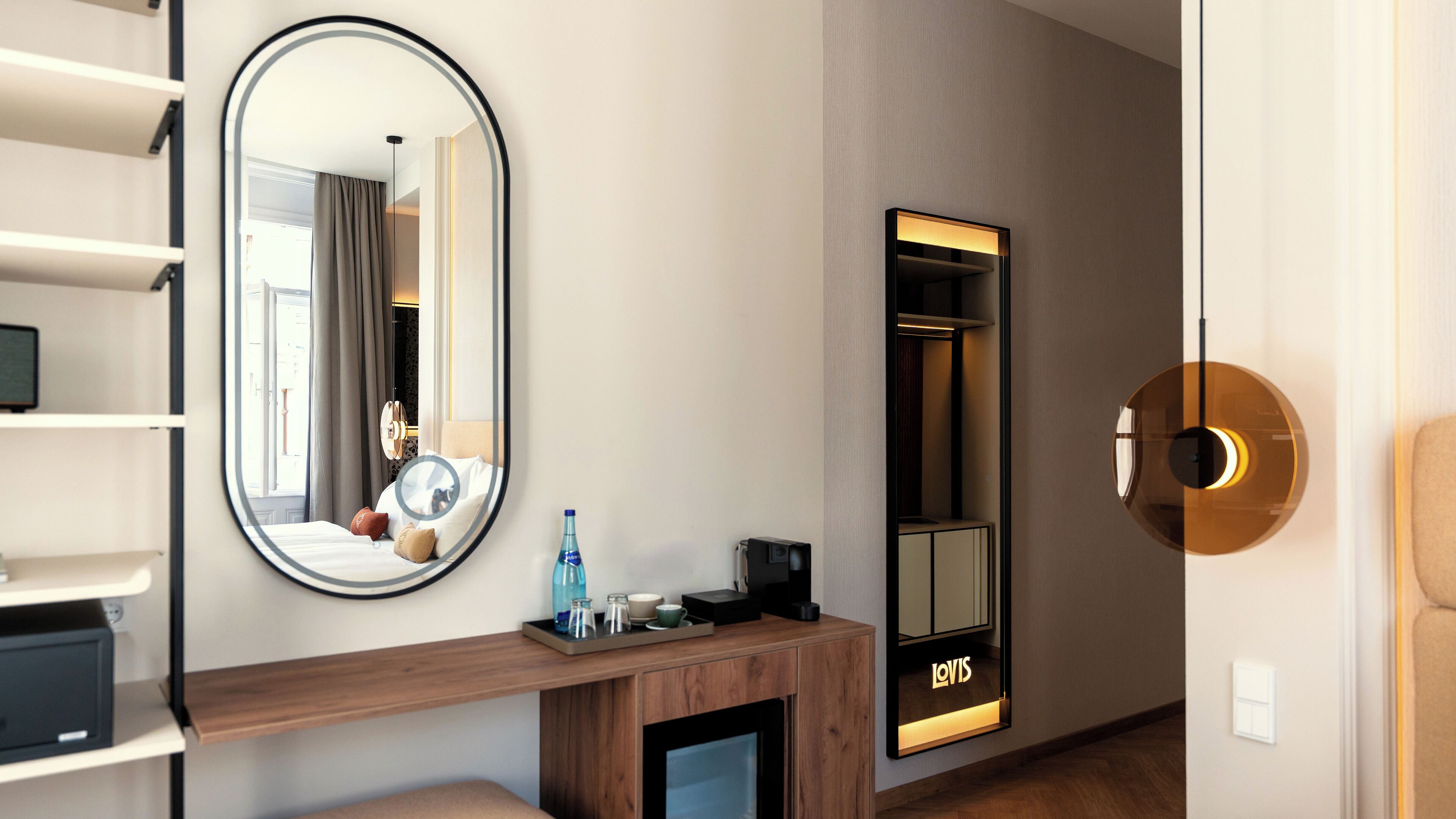 Una habitación de hotel con un espejo grande, un armario, una consola con artículos de aseo y una cama.