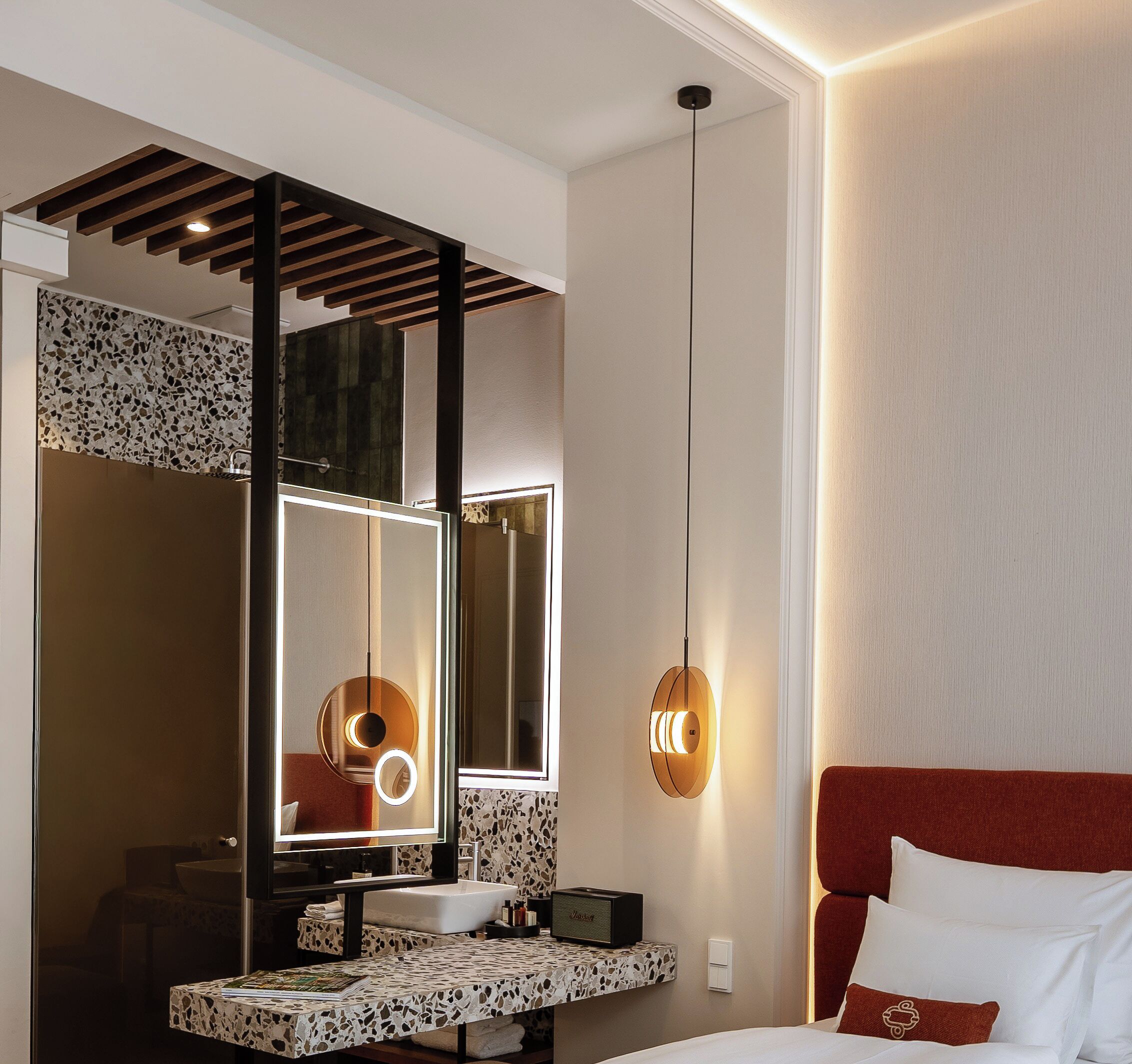 Une chambre d’hôtel moderne dotée d’un grand miroir, d’un lit avec une tête de lit rouge et d’une salle de bain avec un lavabo et un meuble-lavabo.