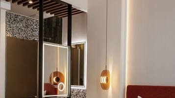 Une chambre d’hôtel moderne dotée d’un grand miroir, d’un lit avec une tête de lit rouge et d’une salle de bain avec un lavabo et un meuble-lavabo.