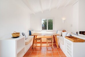 A modern kitchen with a wooden table, two stools, white cabinetry, and a window with a view of greenery. - Casa Maitzgon - Renovated house with pool and garden (Sant Lluís)