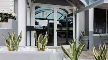 Un edificio moderno con entrada de vidrio, plantas en macetas y barandilla de metal.
