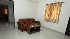 A living room with a brown sofa, a wooden coffee table, and a curtain on the window. - 1 bhk comfy stay 2 (Pune)