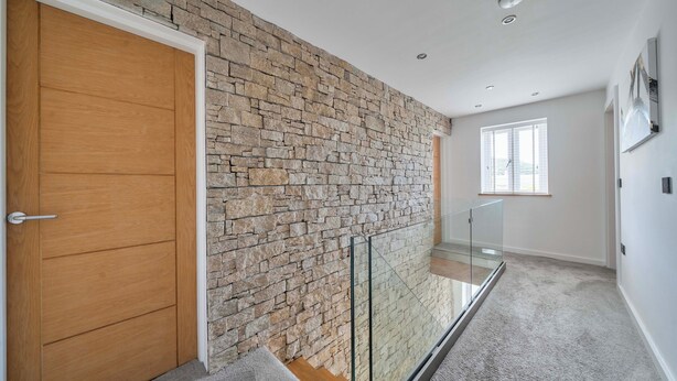 Un interior moderno con pared de piedra, puerta de madera, barandilla de vidrio y una ventana.
