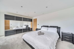 A bedroom with a large bed, a wardrobe with mirrored doors, and a bedside table.