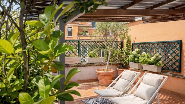 Una veranda riparata con due poltrone bianche, un tappeto decorato e piante in vaso.