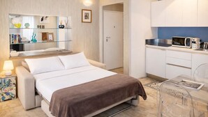 Una camera d'albergo moderna con un letto, un comodino, una lampada e un angolo cottura con forno a microonde.