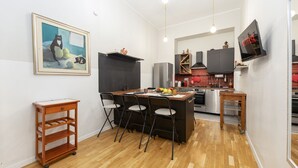Cocina compacta con comedor, una isla negra y televisor instalado en la pared.