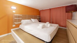 Una habitación de hotel con una cama, cabecera de madera, cortina roja y una lámpara.