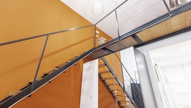 Una escalera con barandillas de metal y escalones de madera, que lleva a una puerta blanca.