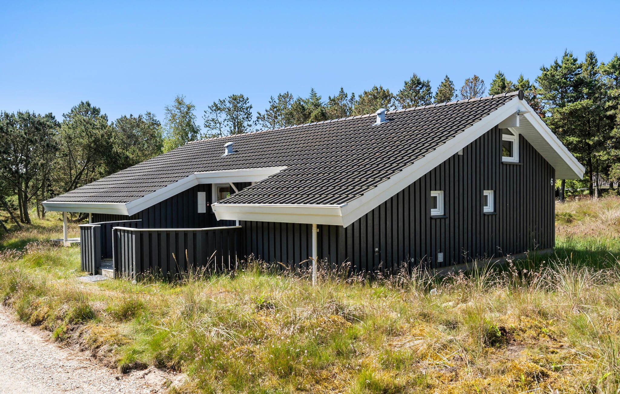 Un bâtiment moderne à deux étages, doté d’un toit en pente, entouré d’un paysage naturel et d’arbres.
