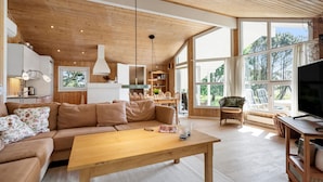 A spacious living room with a wooden ceiling, large windows, a sofa, a coffee table, and a television. - Stunning home in Strandby with WiFi (Strandby)