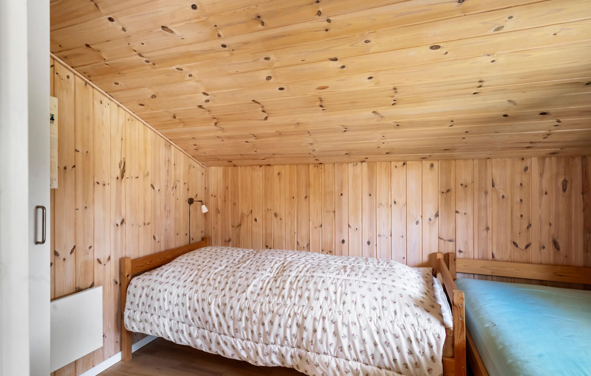 A small, single-bed room with wooden walls and ceiling, a bedside lamp, and a radiator.