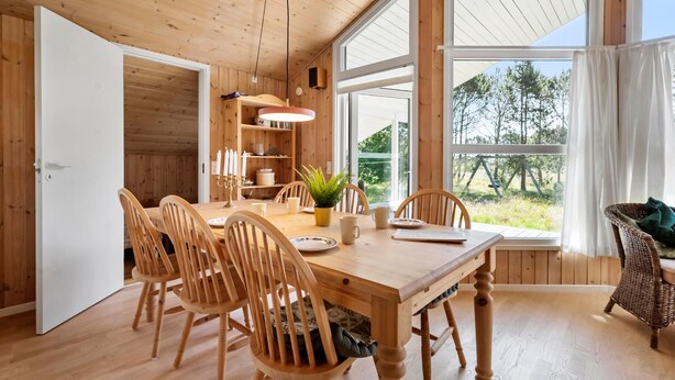 A wooden dining room with a large table, chairs, a potted plant, and a view through large windows. - Stunning home in Strandby with WiFi (Strandby)