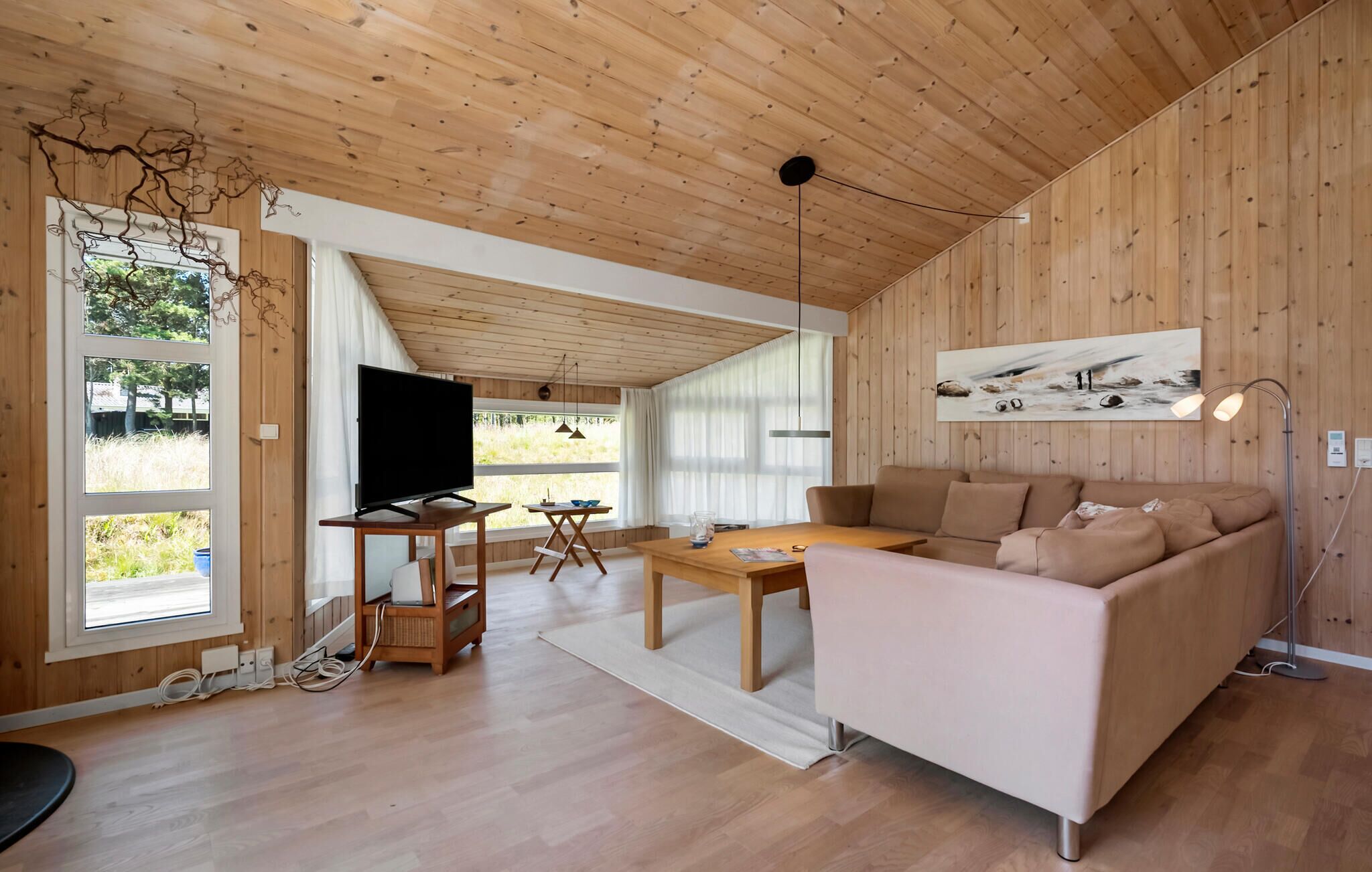 Un salon moderne avec des murs et un plafond en bois, une grande fenêtre, un téléviseur à écran plat, un canapé, une table basse et un tableau accroché au mur.