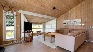 A modern living room with wooden walls and ceiling, a large window, a flat-screen TV, a sofa, a coffee table, and a painting on the wall. - Stunning home in Strandby with WiFi (Strandby)