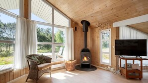 A cozy room with a large window, a fireplace, a wicker chair, and a TV stand. - Stunning home in Strandby with WiFi (Strandby)