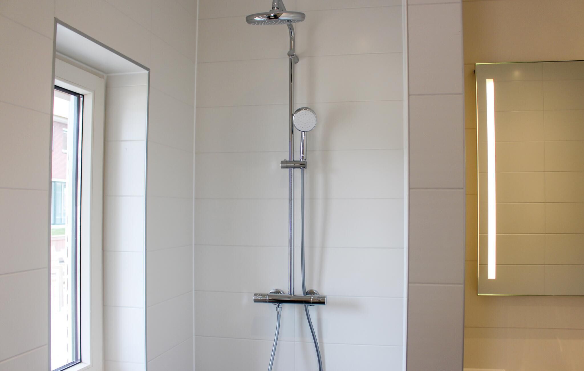 A modern shower with a handheld showerhead and a wall-mounted control panel.