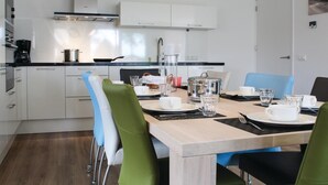 A modern kitchen with white cabinets, a wooden dining table set for four, and a view of the cityscape through the window. - Stunning home in Idskenhuizen with sauna (Idskenhuizen)