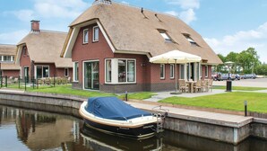 A house with a thatched roof, a boat docked in a canal, and a small outdoor seating area. - Stunning home in Idskenhuizen with sauna (Idskenhuizen)