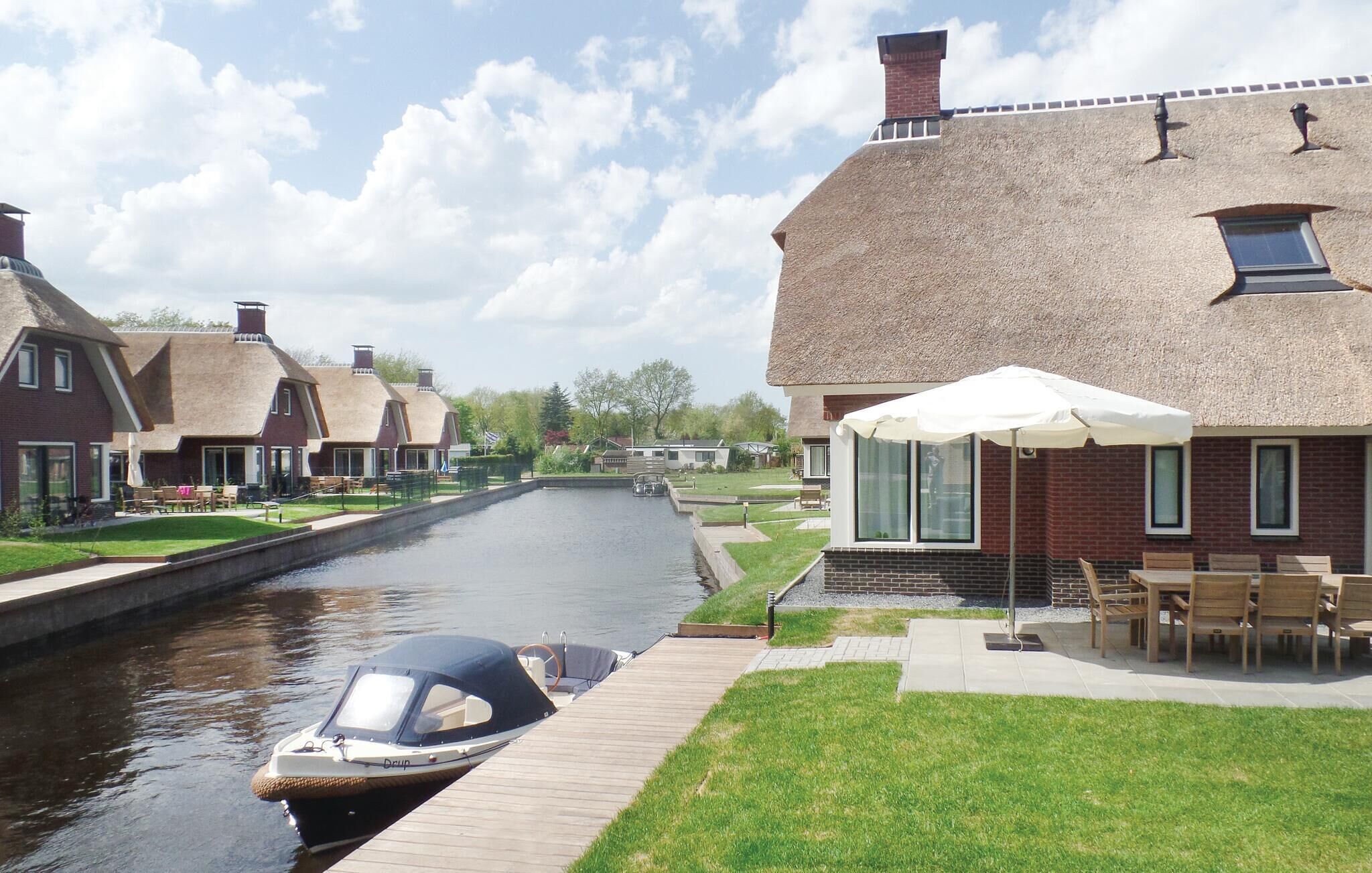 A canal-side property with a boat dock, a patio with outdoor seating, and traditional-style houses with thatched roofs.