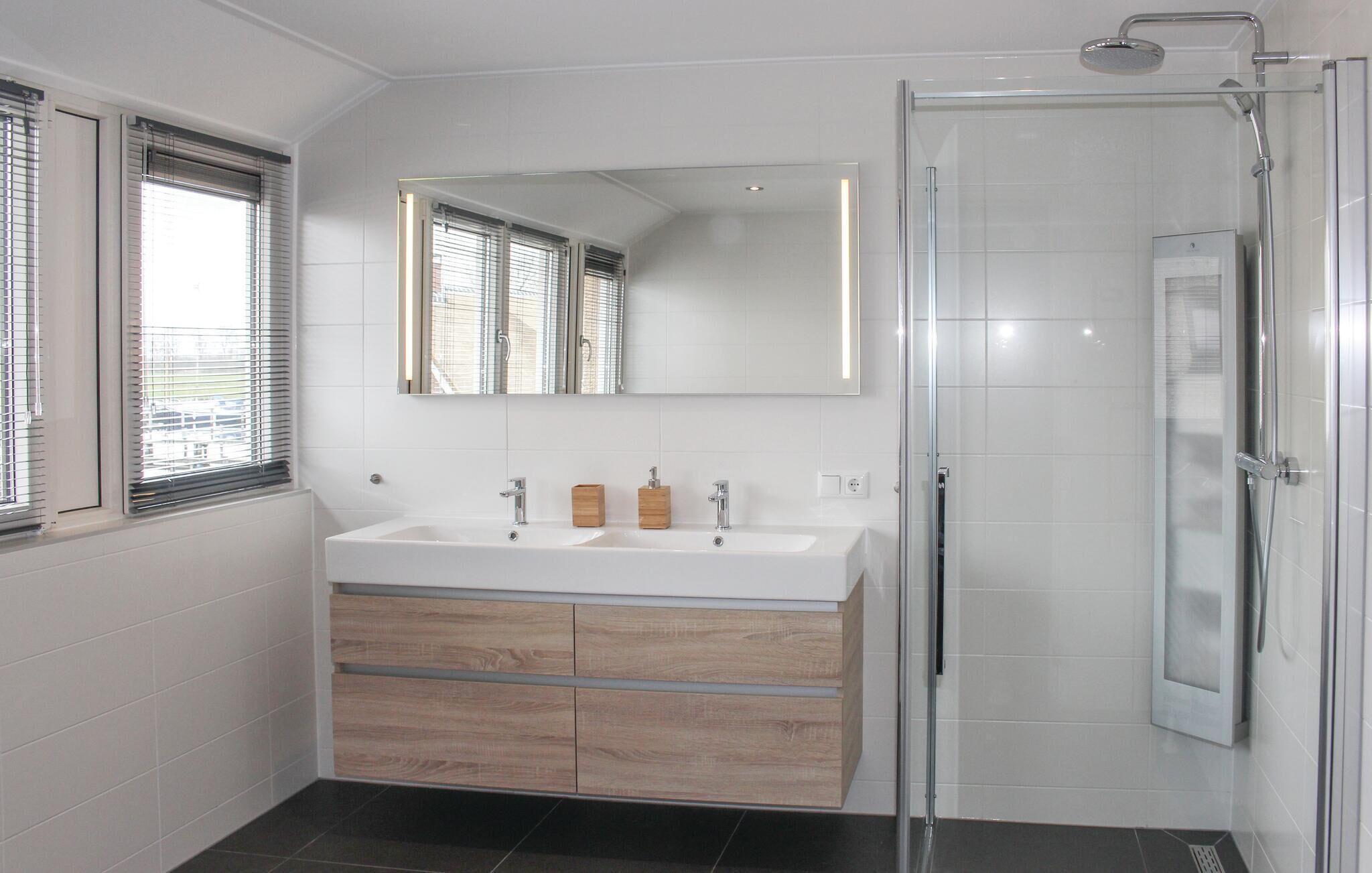 Une salle de bain moderne dotée d’une douche à parois de verre, d’un meuble-lavabo à deux vasques avec des armoires en bois, et d’un grand miroir au-dessus du meuble-lavabo.