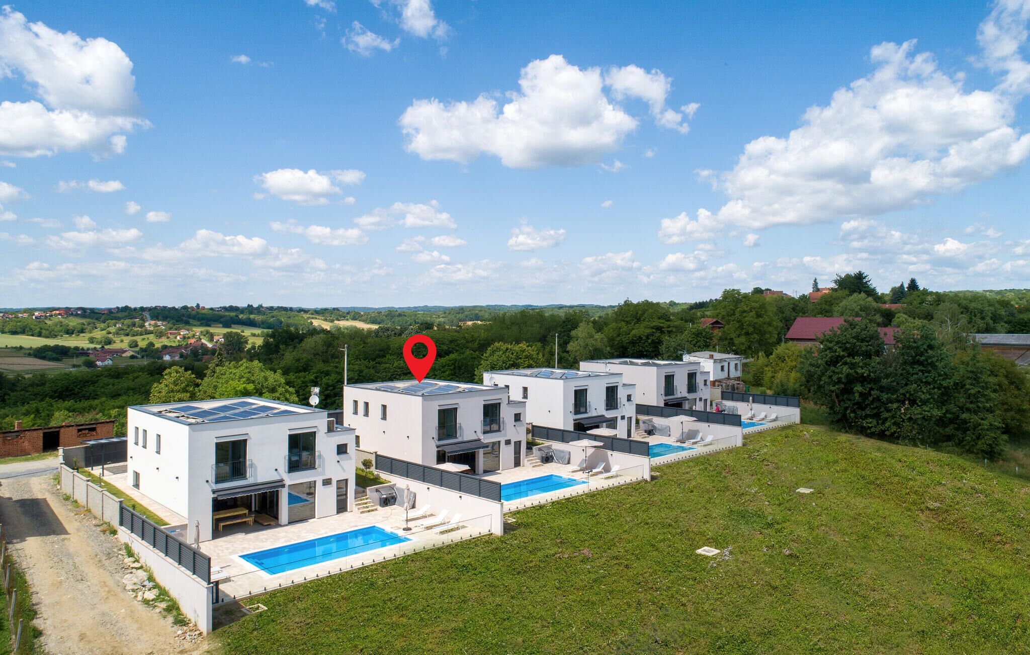 Ein moderner Wohnkomplex mit mehreren weißen Gebäuden, einem Schwimmbecken und einem roten Standortmarker.