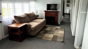 Una sala de estar con un sofá, una chimenea, un televisor y una alfombra.