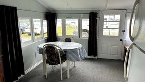 Una habitación pequeña con una mesa redonda y dos sillas, una puerta y ventanas con cortinas.