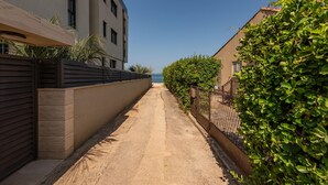 A narrow, paved pathway flanked by modern buildings with a view of the sea in the distance.