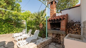 An outdoor patio with stone flooring, a brick oven, and white lounge chairs.